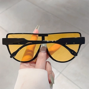 Detail of oversized black pilot sunglasses with transparent yellow lenses held by hand