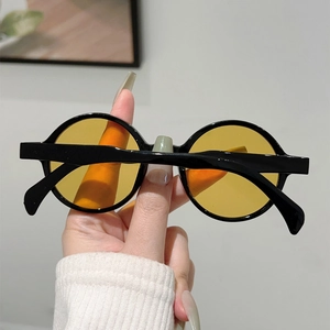 Detail of round frame sunglasses with black thick rims and bright yellow lenses