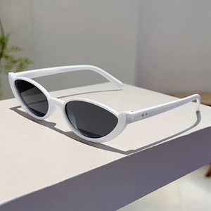 Detail view of white resin cat eye sunglasses with high-quality dark lenses on a grey desk