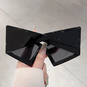 Close-up of black geometric sunglasses with avant-garde X-shaped crossbar bridge design