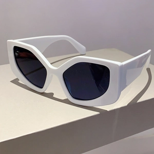 Detail of white geometric cat eye sunglasses featuring dark blue lenses on a beige stand