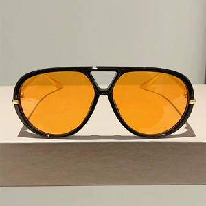 Gros plan de lunettes aviateur avec monture noire et verres orange sur support gris