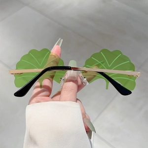 Detailed close-up of green ginkgo leaf shaped frameless sunglasses with gold metal temples