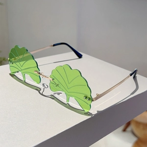 Detailed view of ginkgo leaf shaped frameless sunglasses with green tinted lenses and gold arms