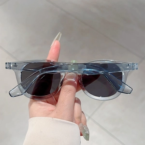 Detail of round vintage sunglasses with transparent blue frame and grey lenses held in hand