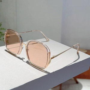 Detail of square gold metal sunglasses featuring light pink lenses on a white display