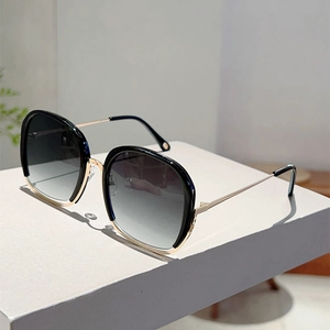 Detail view of square frame sunglasses with gold metal temples on a white stand