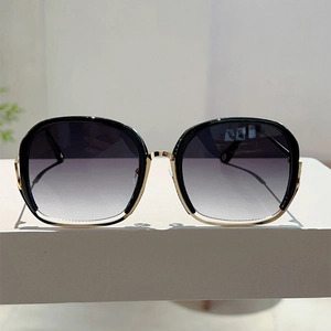 Detail of square black and gold metal sunglasses with gradient lenses on white stand