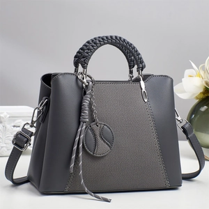 Detail of grey crossbody bag with woven handle, V-shaped stitching and round charm