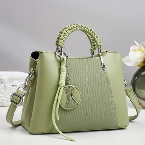 Detail of light green crossbody bag with woven handle and tennis pendant on white surface
