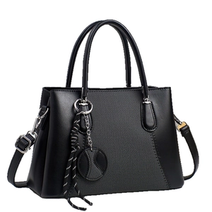 Minimalist black handbag with textured fabric panel and top handles shown on white background