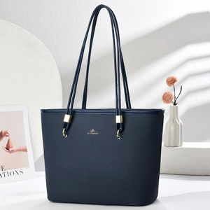 Detailed macro of navy blue textured tote bag with gold hardware and logo in soft light