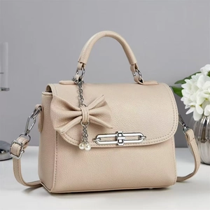 Close-up of beige lychee textured leather bag with silver chain and pearl bow charm