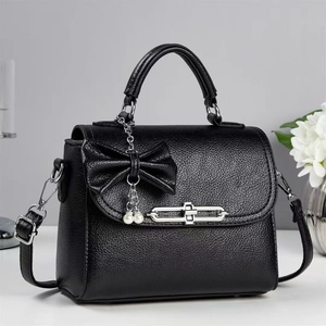 Detail of black lychee grain leather handbag with bow pendant and pearl chain decoration