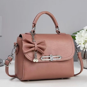 Elegant dusty pink crossbody bag with a bow accent, pearl charm, and pebbled texture