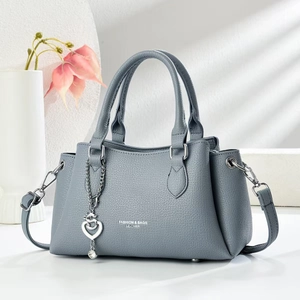 Detail of greyish-blue lychee grain leather handbag with silver heart charm and chain