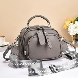 Detailed view of grey pebble leather handbag with wide woven strap and metal hardware