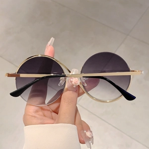 Détail de lunettes de soleil rondes oversize avec verres dégradés violets et monture dorée