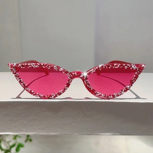 Détail de lunettes de soleil œil de chat rose avec strass sur une surface blanche