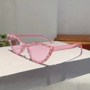 Détail de lunettes de soleil œil-de-chat roses avec strass étincelants sur support blanc
