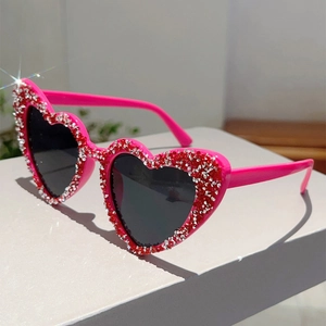 Detailaufnahme der herzförmigen Sonnenbrille mit rosa Rahmen und funkelnden Strasssteinen