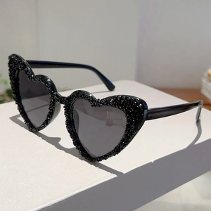 Detail einer herzförmigen Sonnenbrille mit schwarzen Strasssteinen und dunklen Gläsern