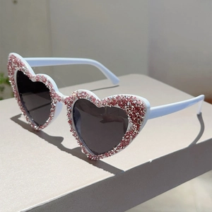 Makroaufnahme einer Herz-Sonnenbrille mit rosa Strasssteinen auf weißem Rahmen