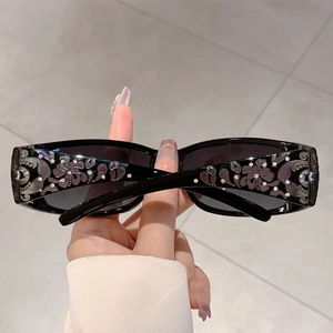 Detail of black rectangular sunglasses with purple floral relief and rhinestones