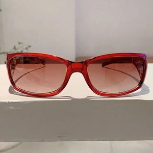Detail of red translucent oval sunglasses with brown gradient lenses on a minimalist stand