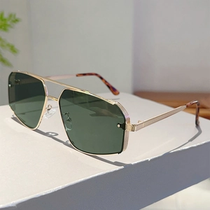 Detail of engraved gold metal temples and green lenses on geometric sunglasses