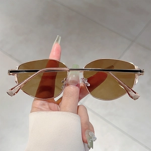 Detail of oval sunglasses featuring tea-brown lenses and gold metal frames held by hand