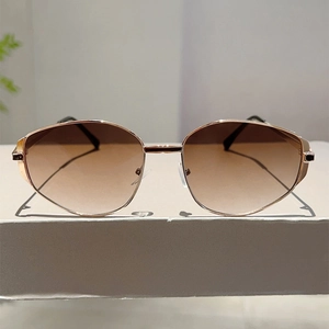 Detailed close-up of polygon gold metal sunglasses with brown gradient lenses on white display