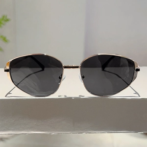 Close-up of golden metal frame sunglasses with dark lenses on a white display stand