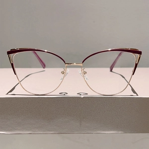 Gros plan de lunettes yeux de chat en métal bordeaux et doré sur support gris