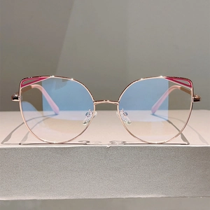 Macro detail of rose gold cat-eye metal frame with blue light blocking lens on grey stand