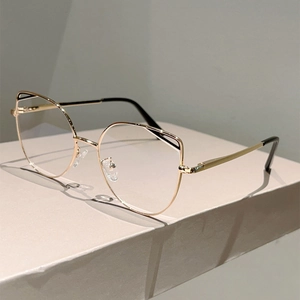 Detail shot of golden cat-eye metal frame with black tips on a minimalist stand