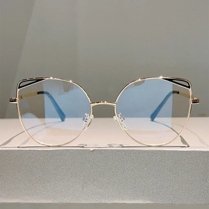 Front view of gold cat-eye glasses frame with blue lenses on a grey display