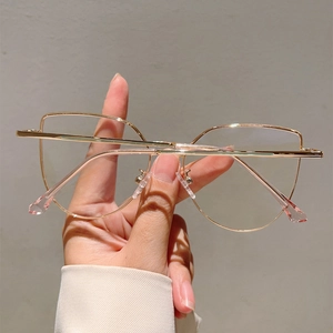 Detail of rose gold geometric oversized metal glasses frame held by hand on grey backdrop