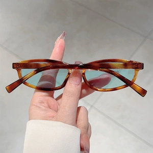 Detailed shot of tortoiseshell cat-eye sunglasses with light blue lenses held in hand