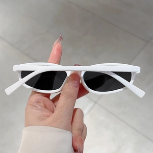 Detail of white oval sunglasses featuring retro narrow frame and dark lenses