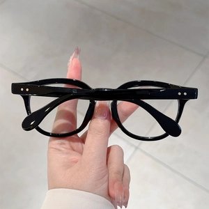 Detail of round black full-frame glasses with retro metal rivets held by hand