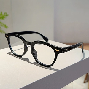 Detailed macro view of black round frame glasses featuring golden wing metal accents