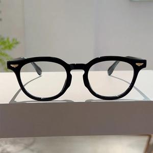 Close-up of black thick-frame glasses featuring gold wing-shaped metal accents on the hinges