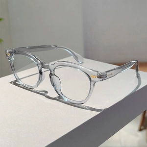 Detail of round transparent grey glasses frame with gold wing metal hinges on white base