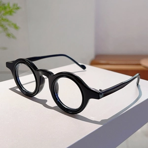 Vue latérale de lunettes rondes noires épaisses sur un support blanc dans un décor épuré