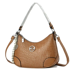 Detail of brown woven shoulder bag with silver circular logo and tassel charm