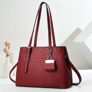Deep red crocodile embossed tote bag with a matching mini charm in a minimalist studio setting