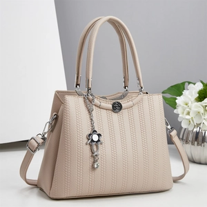 Detalle del bolso beige con textura de panal y un colgante floral de metal