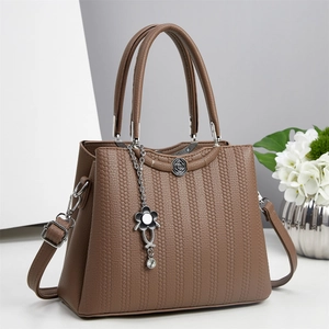 Bolso de mano en cuero marrón con textura tejida y colgante floral, vista de 45 grados