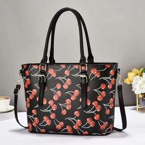 Detail of black tote bag with red cherry pattern, gold hardware and leather texture